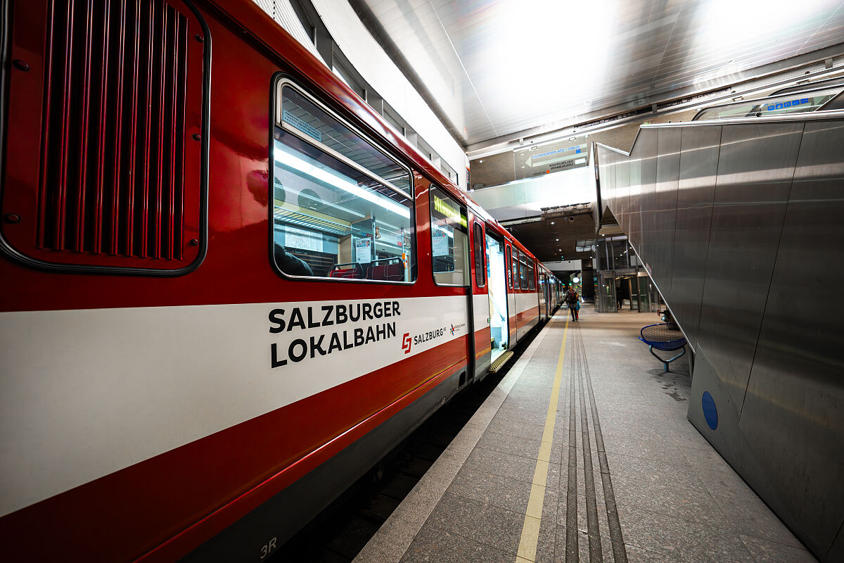 Salzburger Lokalbahn Zug steht am Bahnhof Salzburg Hbf mit geöffneten Türen, eine Person wartet.